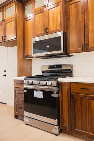 Wood-finish cabinetry with dark hardware, stainless steel appliances, light-toned countertops, and white subway tile backsplash