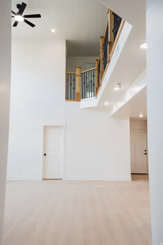 Vaulted ceiling with a ceiling fan, light wood-finish flooring, recessed lighting, and a wood and wrought iron staircase