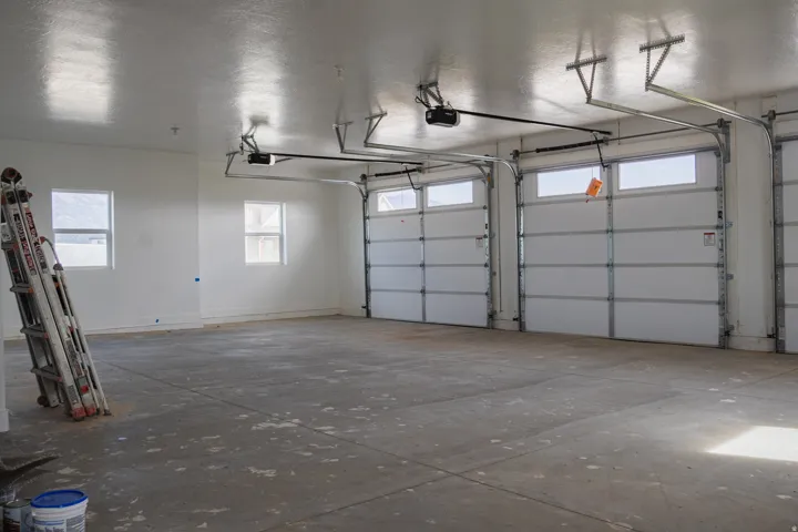 Expansive garage featuring multiple automatic garage doors, concrete flooring, and windows providing natural light