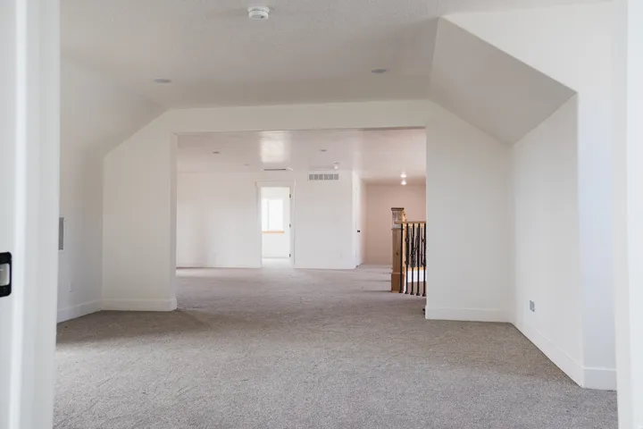 Expansive carpeted area with recessed lighting, angled wall features, and a baluster railing