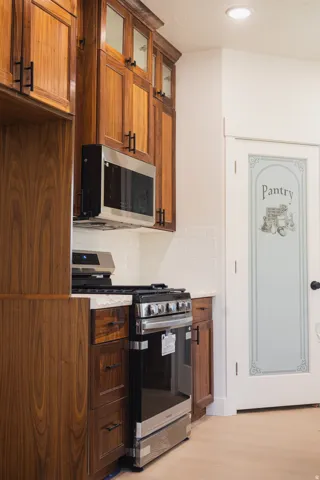 Wood cabinetry with dark hardware, white subway tile backsplash, stainless steel microwave, gas range, and a frosted pantry door