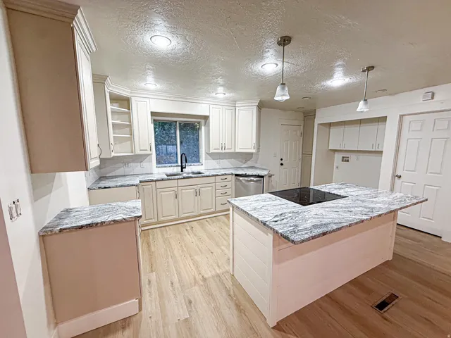 Kitchen featuring shaker-style cabinetry, light-toned wood-finish flooring, recessed lighting, a center island with a cooktop, and light-toned countertops