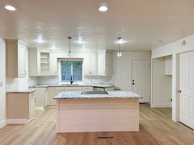 Kitchen featuring wood-finish flooring, white cabinetry, a built-in cooktop, a tile backsplash, and a central island with a stone countertop