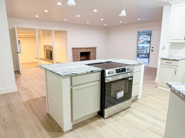 Kitchen island with integrated stainless steel range and cooktop, light-toned cabinetry, and granite-style countertops