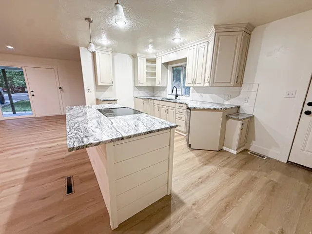 Kitchen featuring an island with a built-in cooktop, light-toned cabinetry, and granite countertops