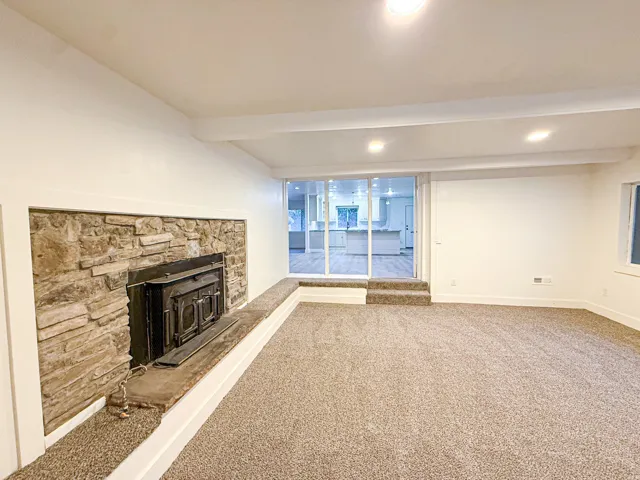 Stone-surround fireplace with a hearth, recessed lighting, carpet flooring, and a sliding glass door