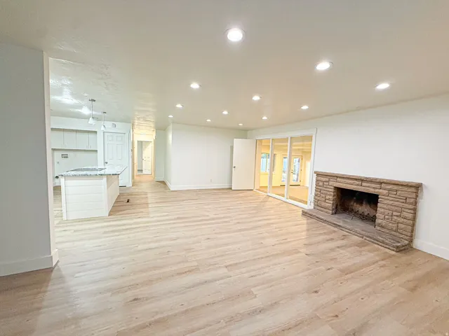 Spacious living area featuring wood-finish flooring, recessed lighting, and a stone-clad fireplace