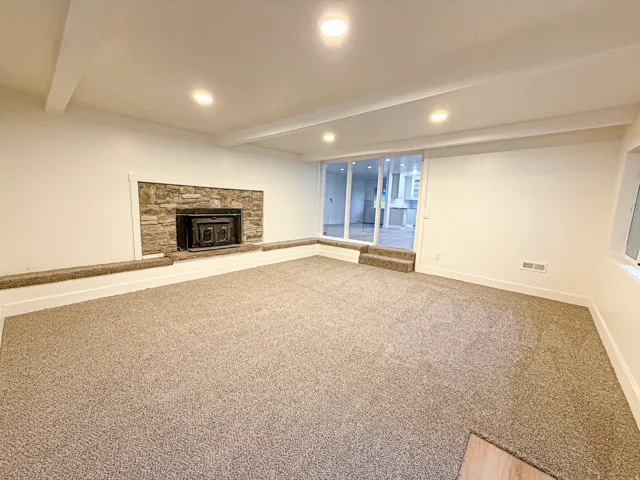 Recessed lighting, exposed ceiling beams, stone-clad fireplace with insert, light-toned carpeting, and a sliding glass door