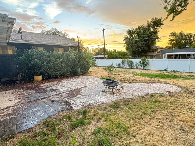 Expansive backyard featuring a stamped concrete patio, dense shrubbery along the perimeter, and a white privacy fence