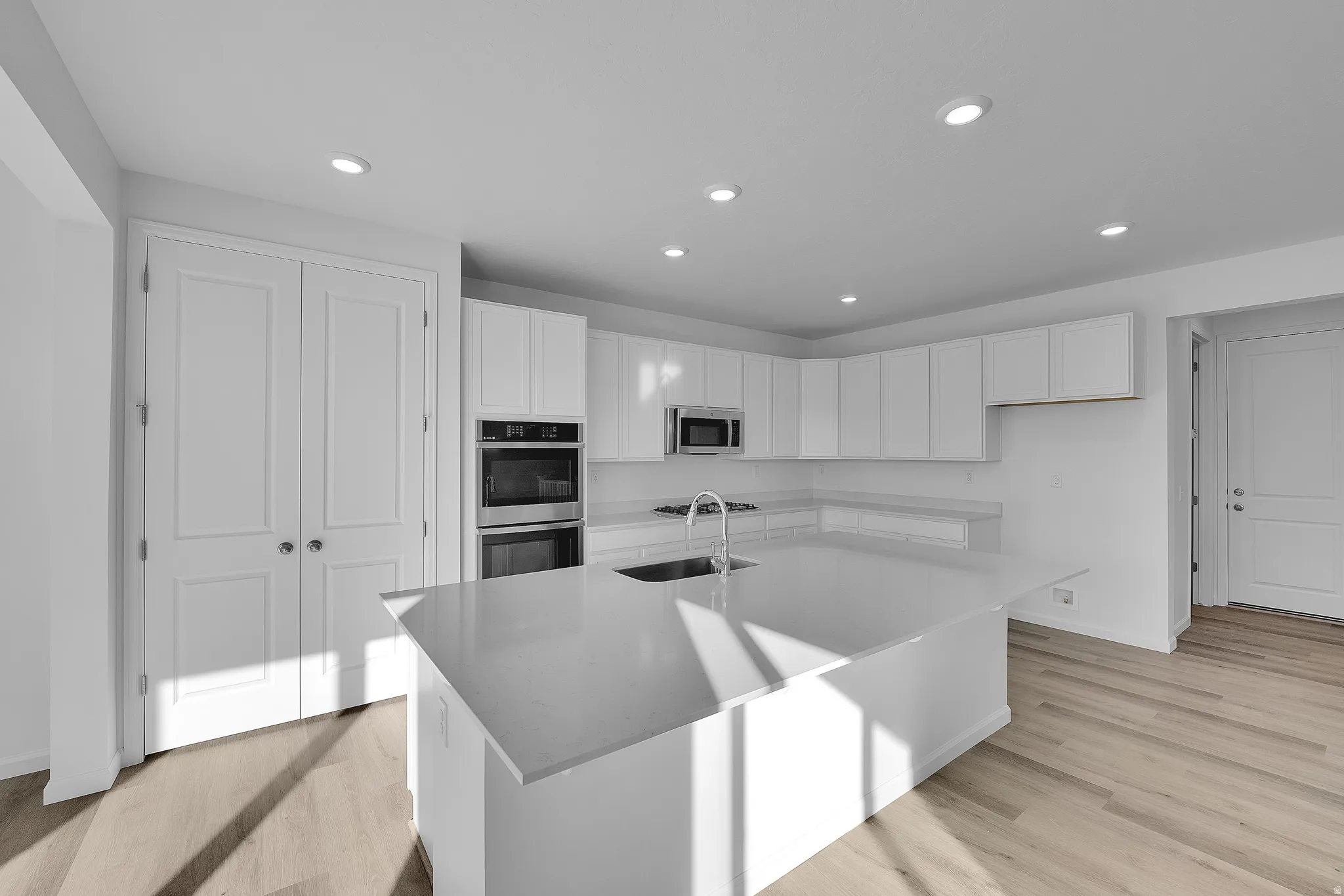Contemporary kitchen with white cabinetry, stainless steel appliances, a large center island, and wood-finish flooring