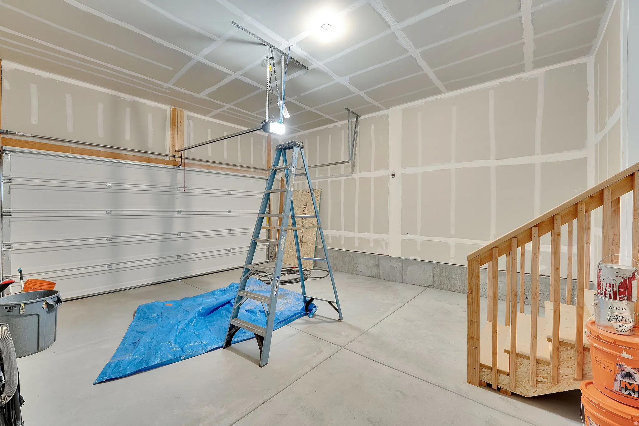 Concrete flooring with a white sectional garage door and unfinished drywall