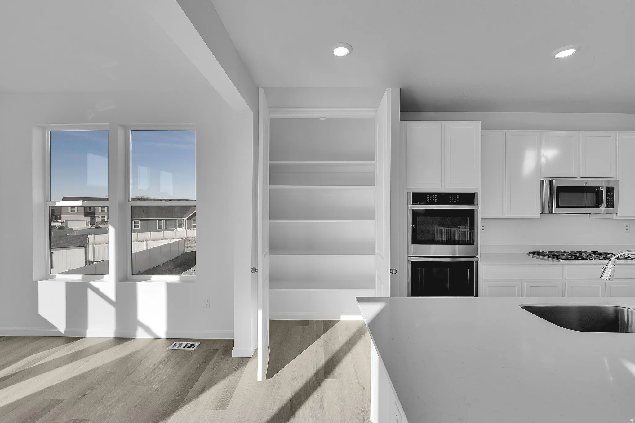 Open-concept kitchen with white cabinetry, stainless steel double ovens, and a built-in microwave