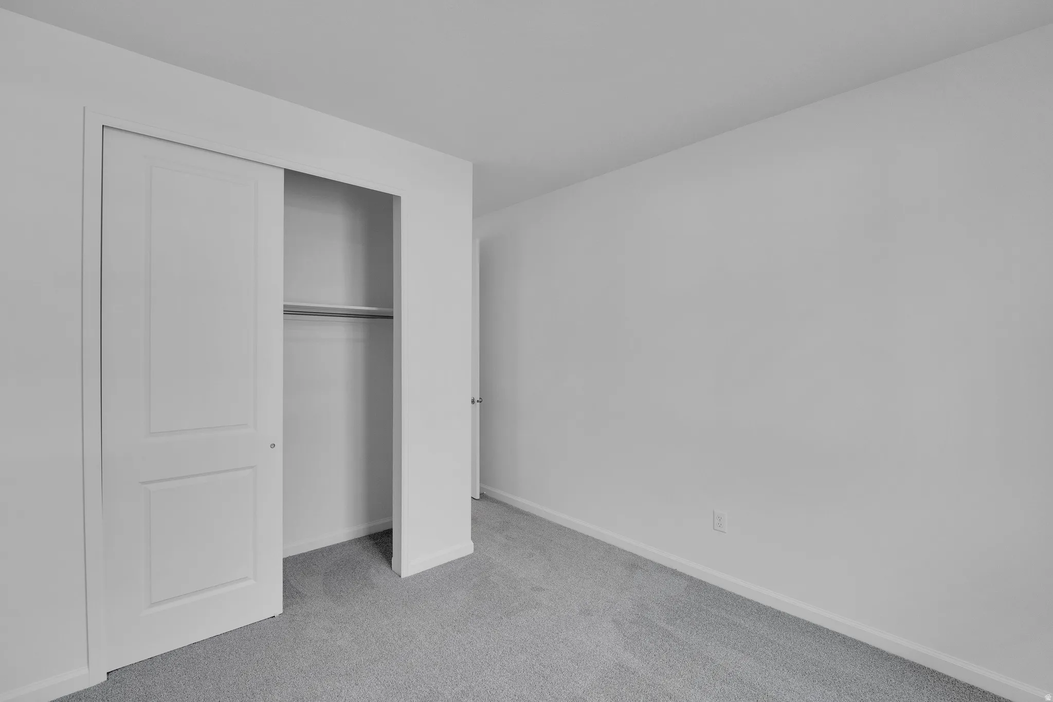 Wall-to-wall carpeting, white painted walls, white trim, and a bi-fold closet door with shelving and a hanging rod