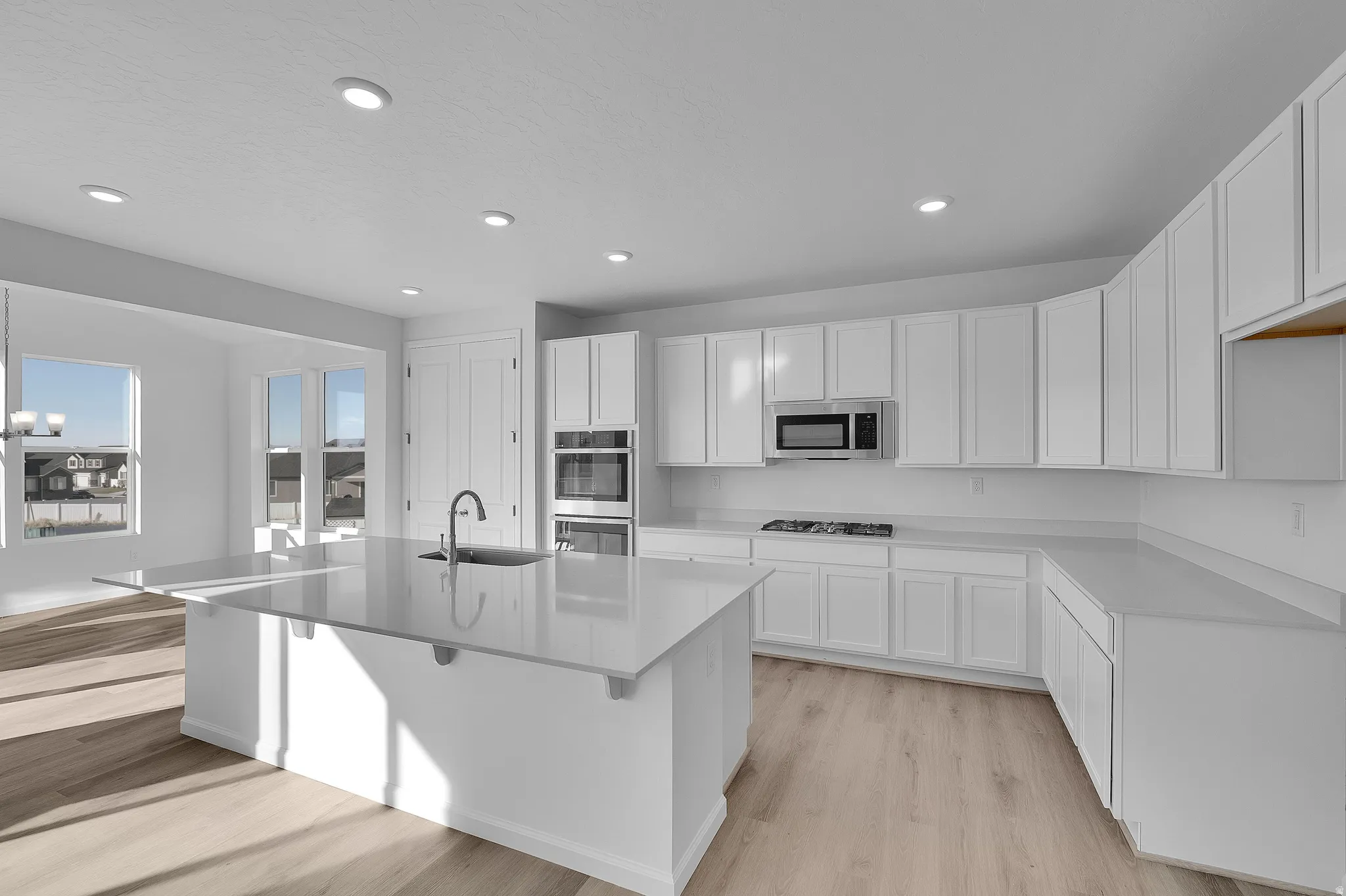 Open-concept kitchen featuring an expansive central island with an undermount sink, white cabinetry, integrated stainless steel appliances, and wood-finish flooring