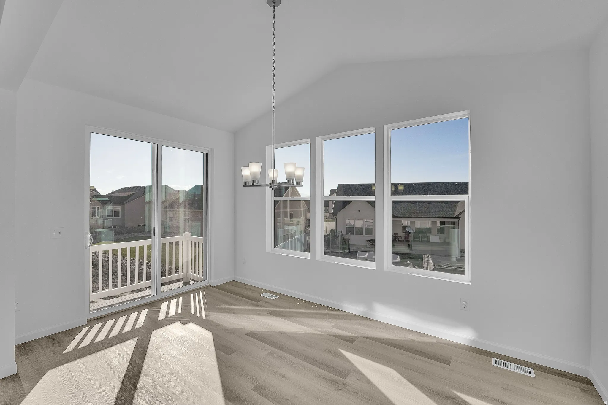 Vaulted ceiling, wood-finish flooring, sliding glass door, white balcony railing, and a multi-light chandelier