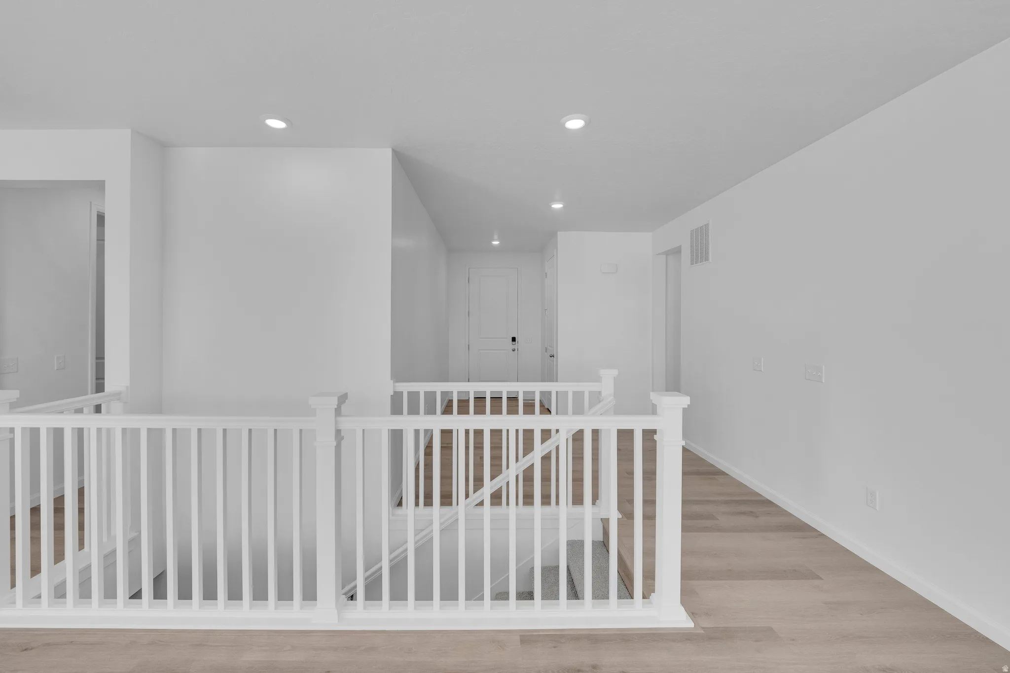 White painted baluster railing, wood-finish flooring, recessed lighting, and white interior doors