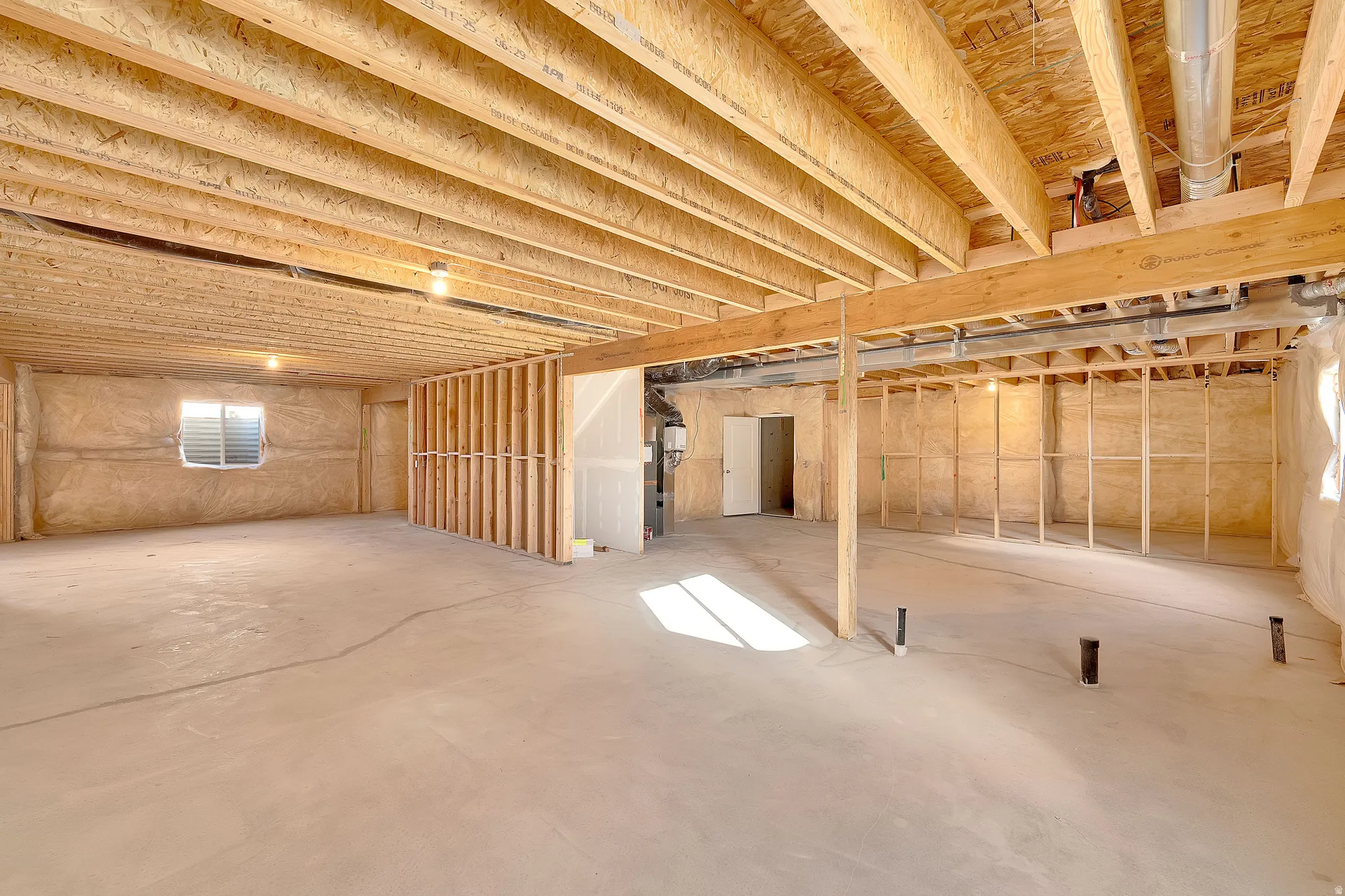 Unfinished lower level featuring exposed wood joists and subfloor, concrete flooring, framing for interior walls, and a window for natural light
