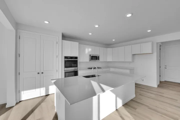 Contemporary kitchen with white cabinetry, stainless steel appliances, a large center island, and wood-finish flooring