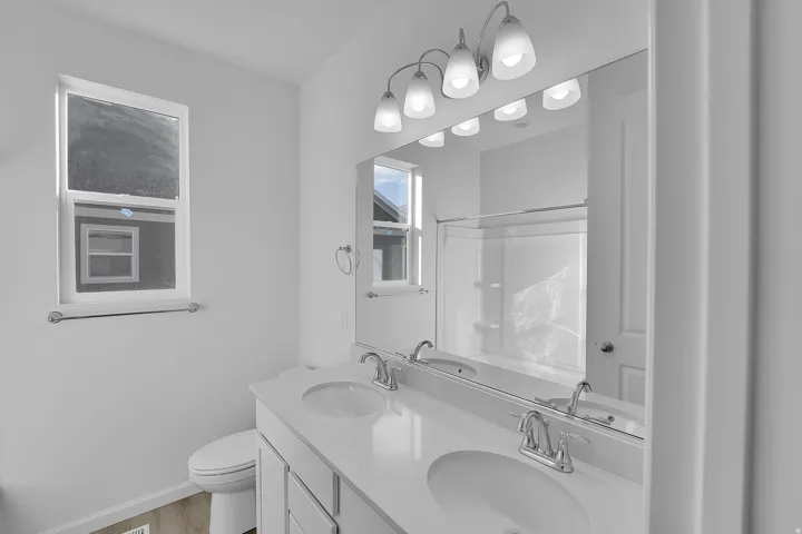 Double vanity with integrated sinks, white cabinetry, chrome fixtures, and a large wall-mounted mirror
