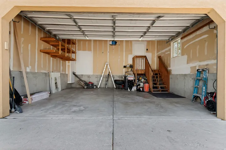 Concrete flooring, overhead storage racks, wooden staircase, upper-level window, and interior access door