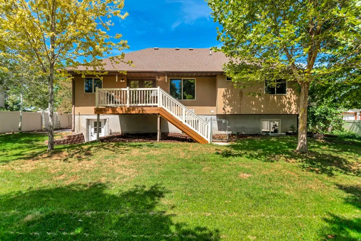 Expansive green lawn with mature trees and a multi-level deck featuring white railings and wood-finish stairs