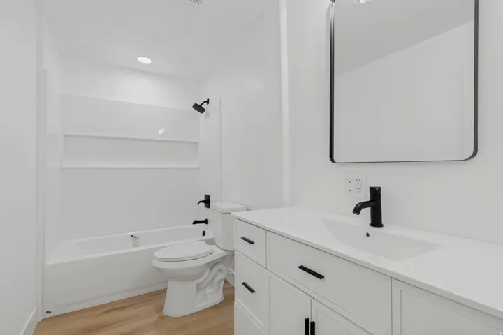 Full bathroom featuring a single vanity with a white countertop, recessed lighting, and wood-finish flooring