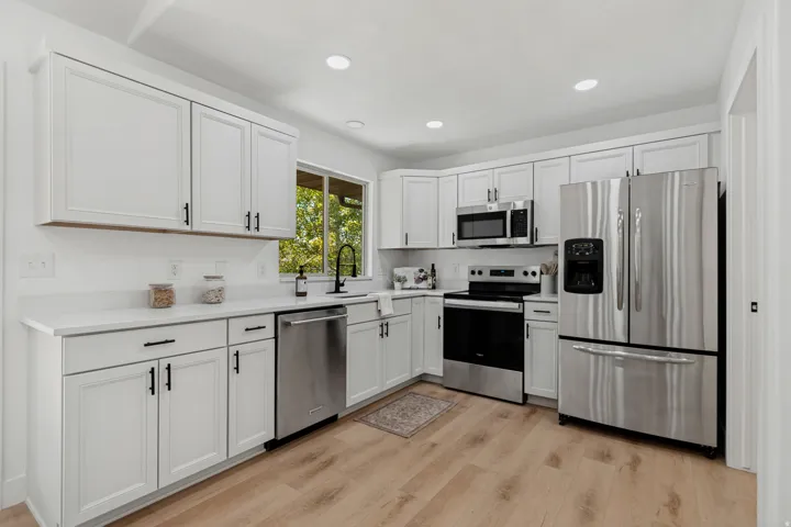 White shaker-style cabinetry, stainless steel appliances, light-toned wood-finish flooring, white countertops, and recessed lighting