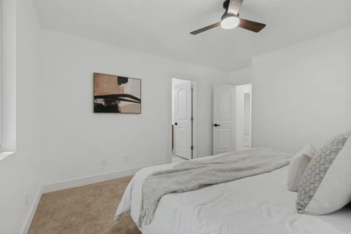 White painted walls, carpeted flooring, a ceiling fan with integrated lighting, and white interior doors with dark hardware