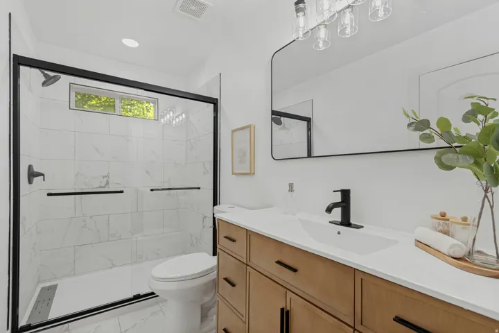 Walk-in shower with black-framed glass enclosure, transom window, and white tile surround