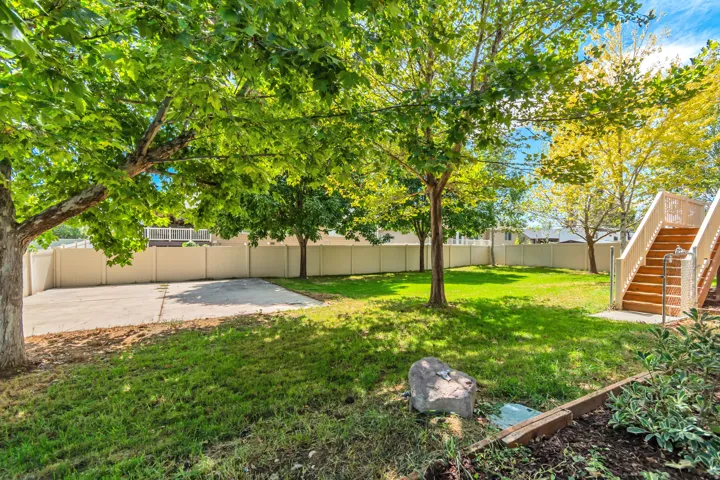 Spacious yard with mature trees, manicured lawn, and a large concrete pad