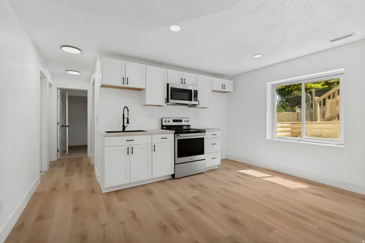 White cabinetry with modern hardware, stainless steel appliances, wood-finish flooring, recessed lighting, and a large window