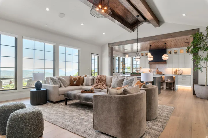 Vaulted ceilings with exposed wood beams, expansive grid-pattern windows, light wood-finish flooring, recessed lighting, and kitchen with under-cabinet lighting