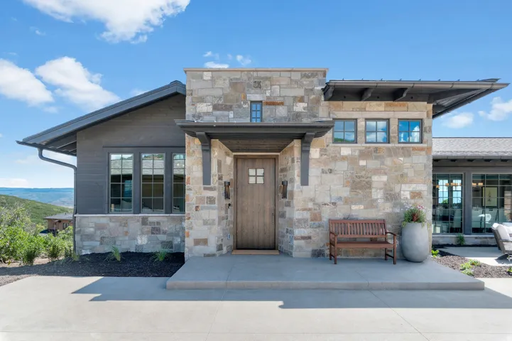 Stone and wood-sided exterior with an angled roofline, a solid wood entry door, and dark-framed windows