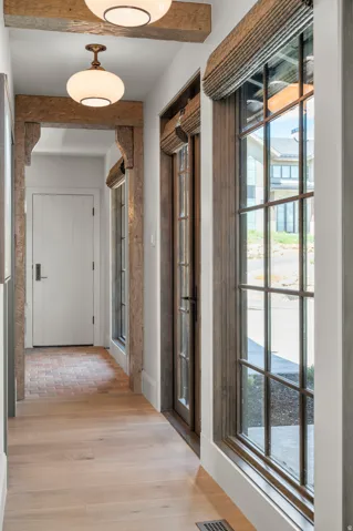 Hallway featuring exposed wood beams, bronze-finish pendant lighting, wood-finish flooring, and multiple paned windows