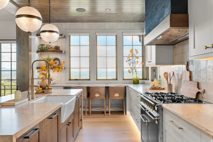 Gourmet kitchen with a farmhouse sink, light wood-finish flooring, custom range hood, and three large windows