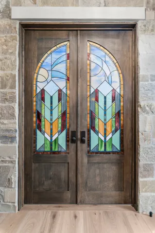 Double entry doors with stained glass inserts, stone surround, and light wood-finish flooring