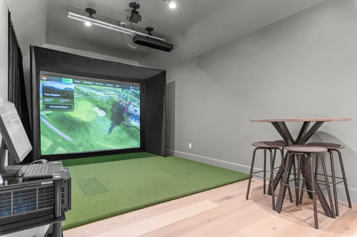Golf simulator with a large projection screen, dedicated turf flooring, overhead projector, and wood-finish flooring