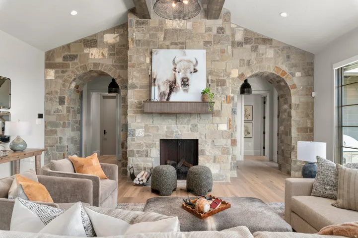 Stone-clad fireplace with a wood mantle, vaulted ceilings with exposed beams, light wood-finish flooring, and arched stone doorways