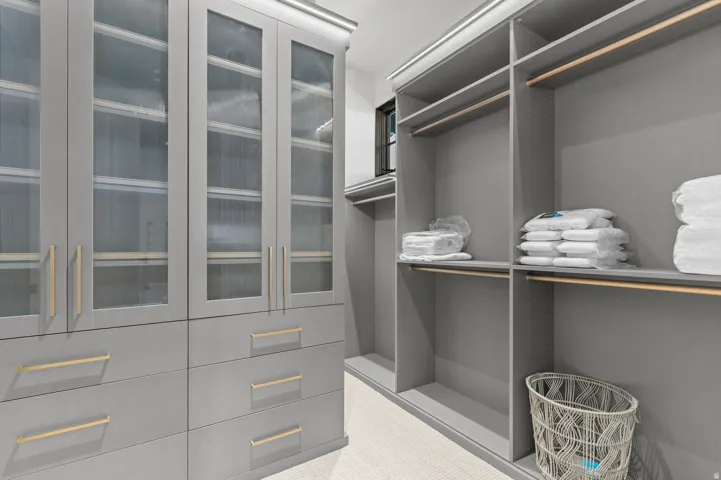 Built-in closet system featuring grey cabinetry, glass-front upper cabinets, and gold-tone drawer pulls
