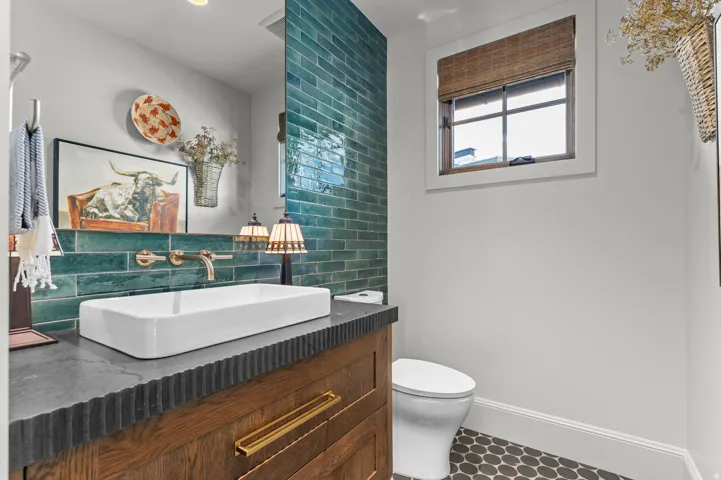 Rectangular vessel sink with wall-mounted brass faucet, wood vanity with textured countertop, teal subway tile accent wall, and hexagonal floor tiles