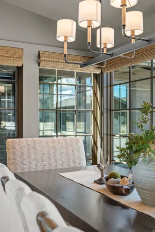 Black metal chandelier with fabric shades, wood-finish dining table, and large window panels