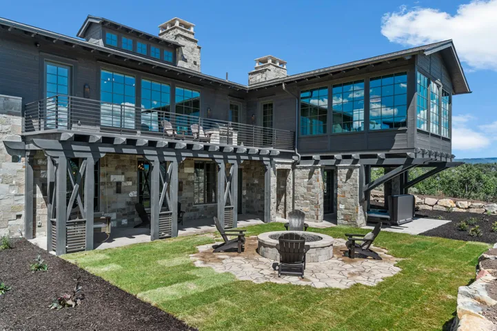 Multi-level exterior featuring stone and wood siding, a second-story balcony with metal railings, and an expansive lower patio with a built-in fire pit