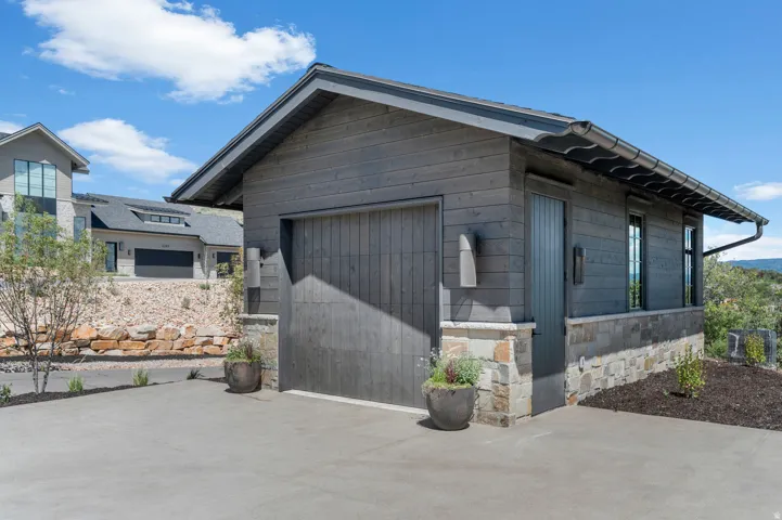 Wood-finish siding, stone accents, concrete driveway, attached garage, and exterior lighting
