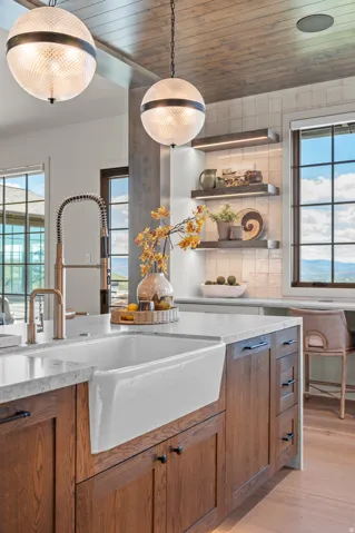 White farmhouse sink with a gooseneck faucet, light-toned countertop, and wood-finish cabinetry