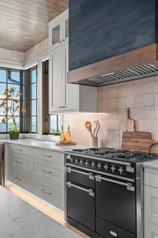 Custom range hood with wood accent, professional-grade range, tiled backsplash, white cabinetry, and light-toned ceiling