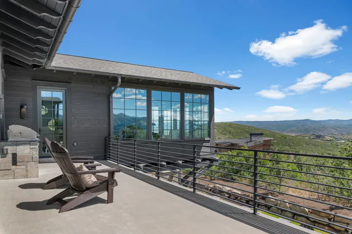 Exterior deck with a stone-clad built-in grill station, multiple windows, and a metal railing