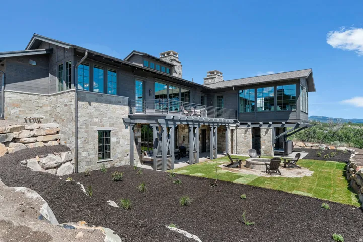 Stone and wood-clad exterior with a covered patio, upper-level balcony, and a built-in fire pit