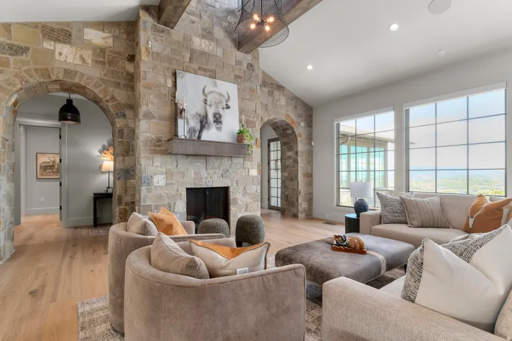 Stone fireplace with a wood mantel, vaulted ceiling with exposed wood beams, and a black wrought iron chandelier