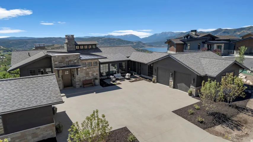Stone and wood-sided exterior with a multi-car garage, expansive driveway, and a prominent chimney feature