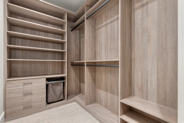 Custom closet system featuring wood-finish cabinetry, integrated shelving, pull-out drawers, and black metal hanging rods